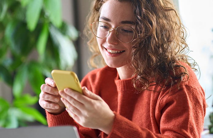 "Mujer joven sonriendo mientras interactúa con su teléfono móvil, representando el engagement en una estrategia de contenidos digitales.